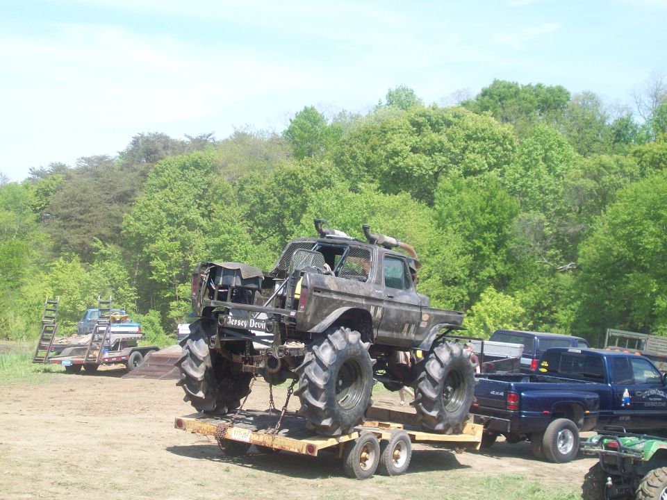 Monster truck with large tires on a trailer, a blue pickup truck is behind it