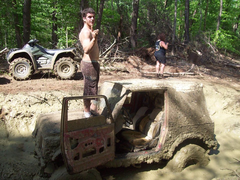 Mud-covered SUV interior stuck in a ditch, ATV nearby