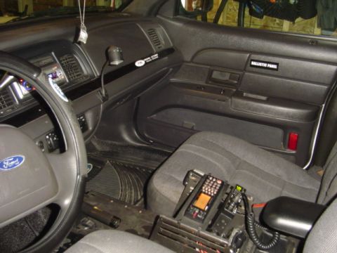 2003 Ford Crown Victoria - The interior of a 2003 Ford Crown Victoria police car is visible, equipped with police radio equipment and a "BALLISTIC PANEL" label on the…