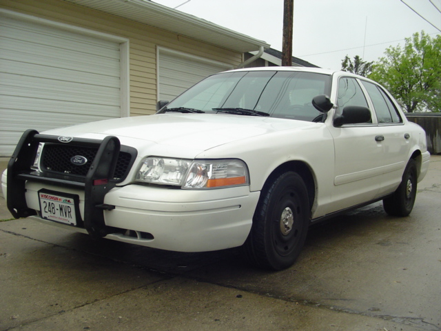 White Ford Crown Victoria police car with a push bumper parked in front of a garage