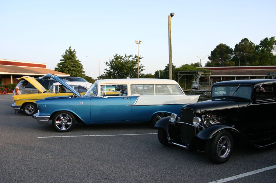 Blue and white station wagon parked next to a yellow sedan and a black hot rod