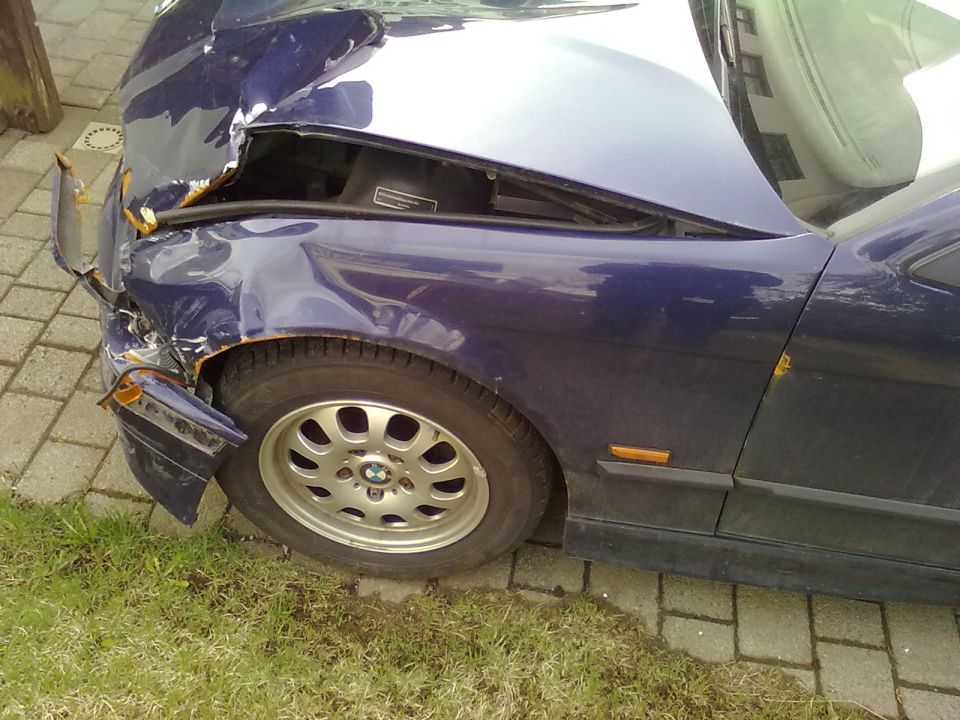Damaged blue 1998 BMW 3 Series, front fender and hood crumpled, tire visible