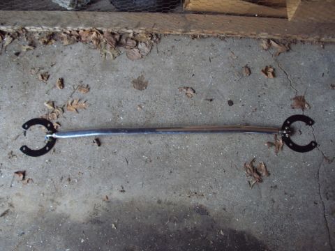 1993 Ford Probe - A chrome strut bar with black horseshoe-shaped mounting brackets lies on a concrete surface.
