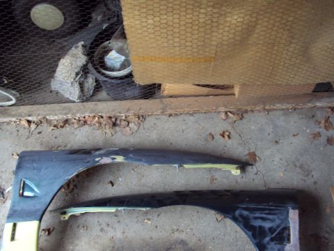 1993 Ford Probe - Two car fenders are shown, one with yellow trim and the other a dark color, lying on a concrete surface.