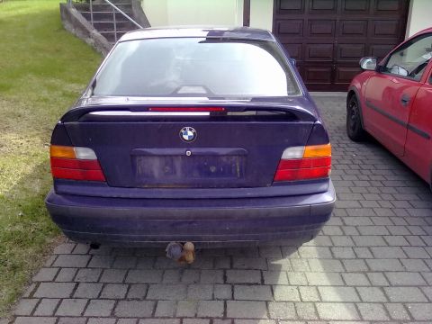 1998 BMW 3 Series - The rear of a dark blue BMW sedan is shown, parked on a brick driveway next to a red car.