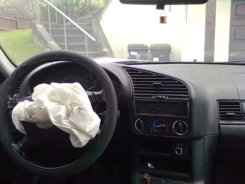 1998 BMW 3 Series - The interior of a car shows a deployed airbag on the steering wheel and the dashboard with air vents and controls.