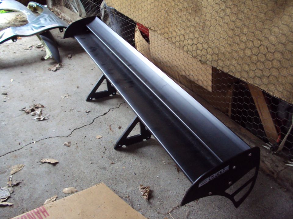 Black aftermarket car spoiler with "CKT" logo on a concrete floor