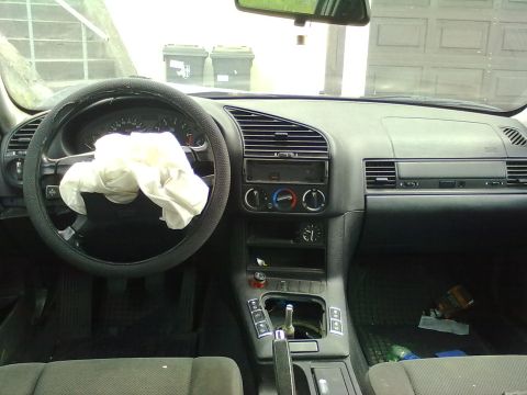 1998 BMW 3 Series - The interior of a car shows a deployed airbag and a water bottle on the floor.