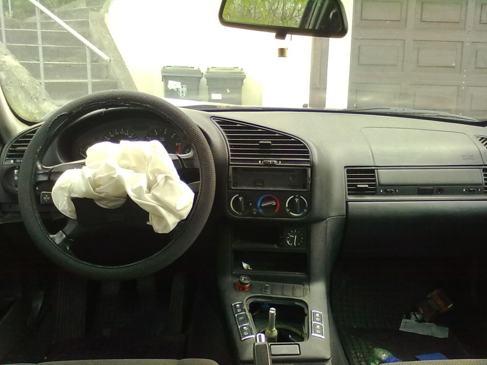 Interior of a 1998 BMW 3 Series with deployed driver airbag and some items on the passenger floor