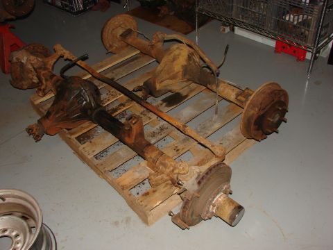 1993 Jeep YJ - Two old, rusty vehicle axles are stored on a wooden pallet in a garage or workshop.