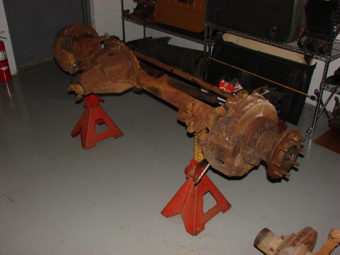 1993 Jeep YJ - A heavily rusted front axle assembly is displayed on jack stands indoors.