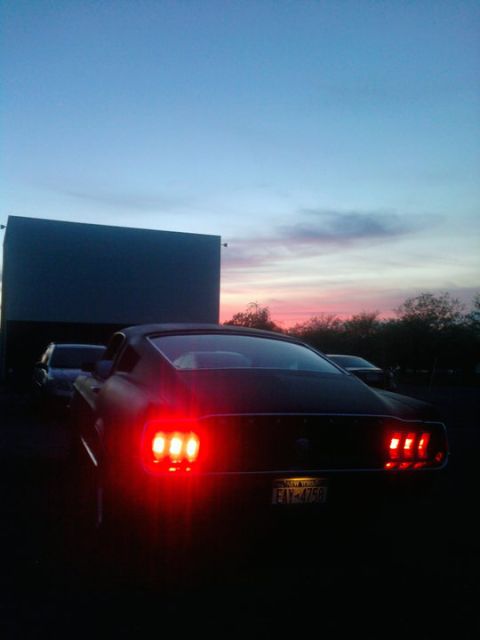 1968 Ford Mustang - A classic Mustang's taillights glow red against the twilight sky at a drive-in theater, with a movie screen in the background.