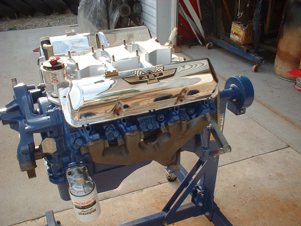 Ford 427 engine with chrome valve covers on a blue engine stand in a driveway