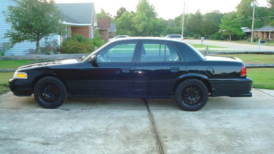 Black Ford Crown Victoria sedan, side view, black aftermarket wheels, parked in driveway