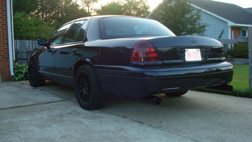 Black four-door sedan with blacked-out wheels parked on a driveway, rear view