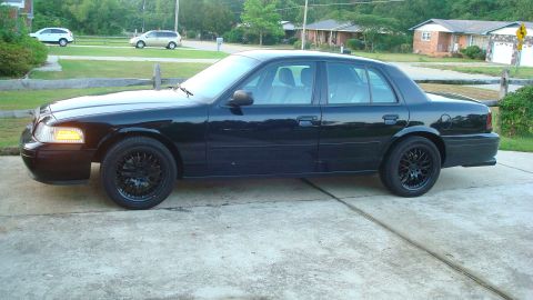 2004 Ford Crown Victoria - A black sedan is parked on a concrete driveway in front of a residential house.
