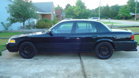 2004 Ford Crown Victoria - A black 2004 Ford Crown Victoria is shown from the side, parked on a concrete driveway in front of a house.