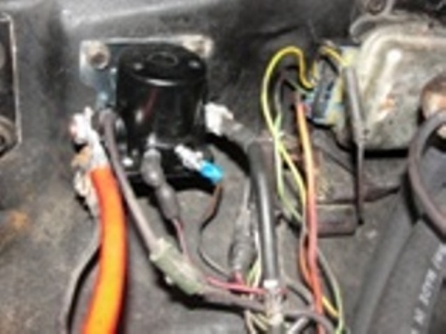 Black starter solenoid on bracket in engine bay with orange cable and assorted wiring