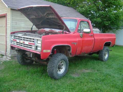1985 Chevrolet C/K Pickup - This red 1985 Chevrolet C/K Pickup is shown with its hood open, revealing the engine bay.