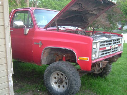 1985 Chevrolet C/K Pickup - This 1985 Chevrolet C/K Pickup is red and has its hood open while parked on grass.