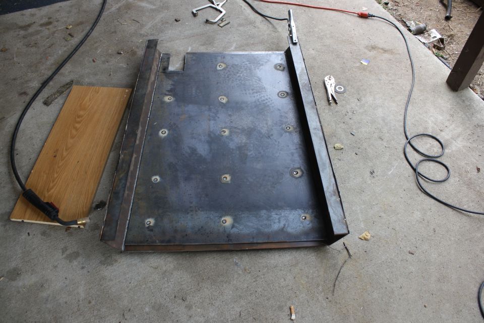 Metal plate with bolt heads, on concrete floor next to wood plank and welding equipment
