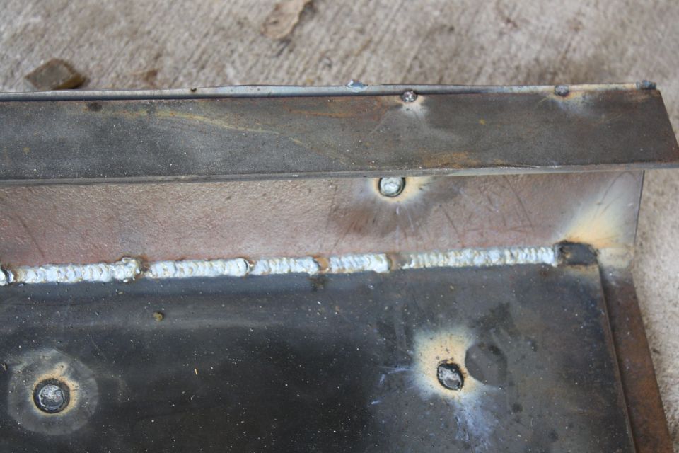 Close-up of welded metal plates with visible weld beads and some circular indentations