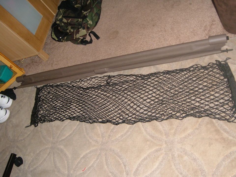 Tan retractable cargo cover canister and black mesh cargo net laid out on carpet