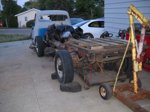 1954 Ford F-100 - A disassembled truck chassis, likely from the 1950s, sits on a concrete driveway with an engine mounted.