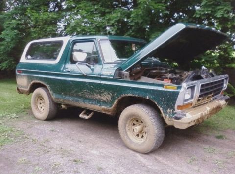 1979 Ford Bronco - Mud-covered 1970s Ford Bronco parked outdoors with its hood up, revealing the engine compartment.