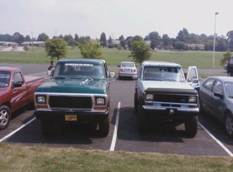 1979 Ford Bronco - Two Ford trucks are parked in a lot, one green and one light blue, with other vehicles in the background.