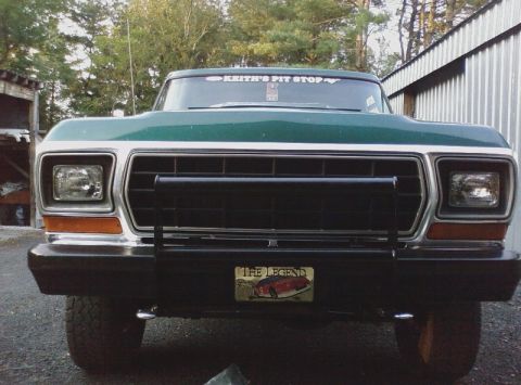 1979 Ford Bronco - Front view of a green truck, possibly a 1979 Ford Bronco, a prominent black grille and bumper with a decorative license plate.