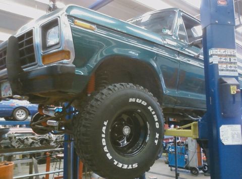 1979 Ford Bronco - A green Ford pickup truck is raised on a hydraulic lift in a garage, revealing its undercarriage and large tires.