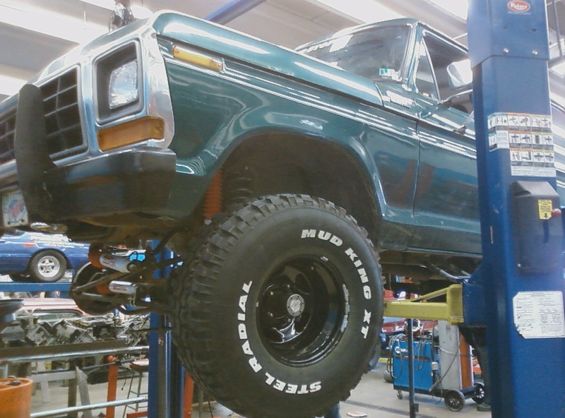 Green Ford pickup truck on a lift, showing front end and side profile. Tires say Mud King XT