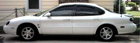1997 Ford Taurus - A white sedan is parked on a driveway in front of a residential building.