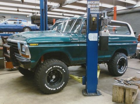 1979 Ford Bronco - Green 1978 Ford Bronco with white top and off-road tires is raised on a hydraulic lift in a garage.