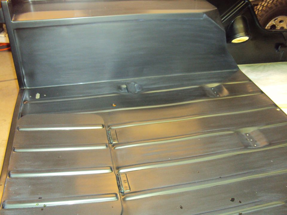 Close-up of a ribbed metal floor pan, possibly from a vehicle. A black vent pipe is visible on the right