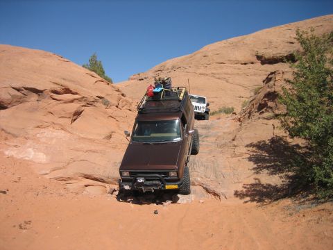 1986 Ford Bronco II - Two off-road vehicles navigate a steep, rocky path under a clear blue sky.