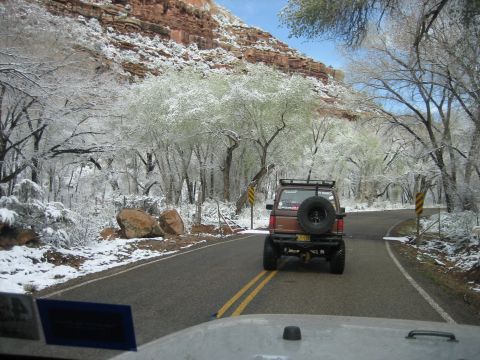 1986 Ford Bronco II - A brown SUV drives on a road through a landscape with snow on the trees and ground.
