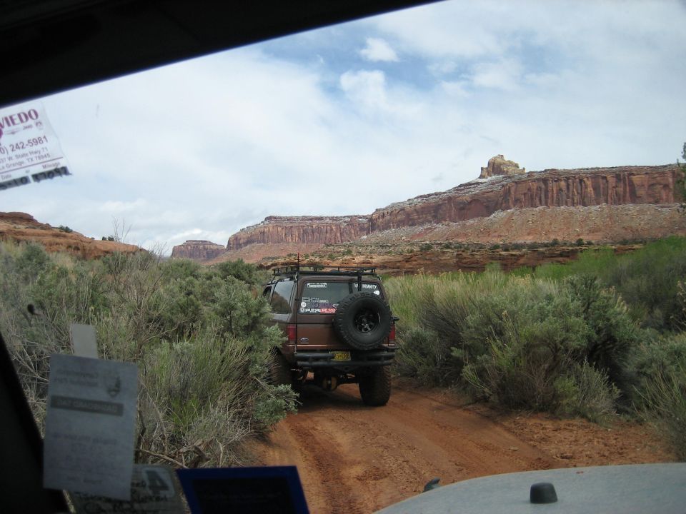 Brown 1986 Ford Bronco II driving on a dirt road in a canyon