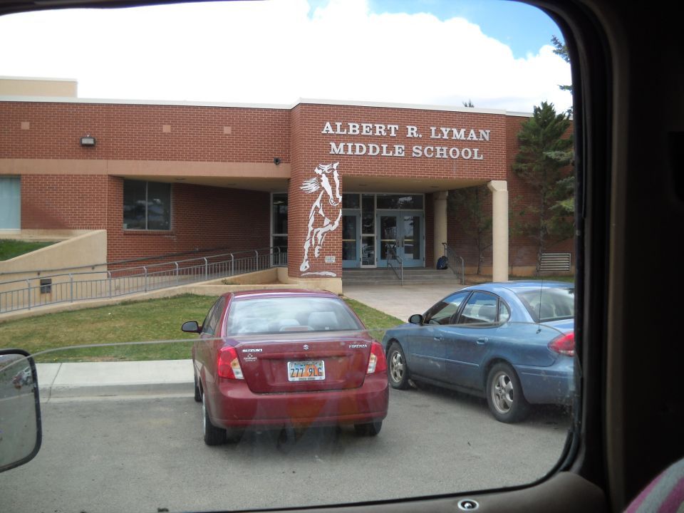 Albert R. Lyman Middle School building entrance with a red sedan and a blue sedan parked outside