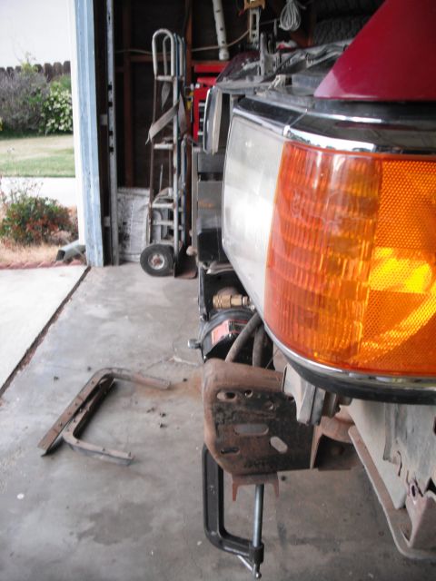 1991 Ford Bronco - A detached front bumper bracket is clamped to the frame of a vehicle in a garage.
