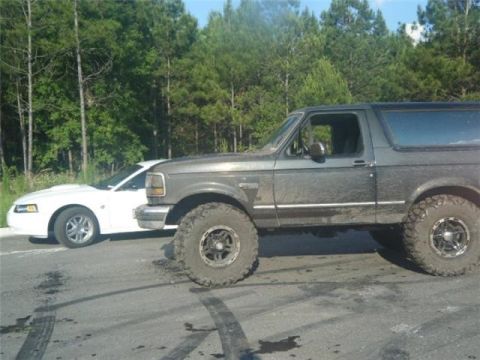 1994 Ford Bronco - A lifted 1994 Ford Bronco sits on a muddy road next to a white sports car.