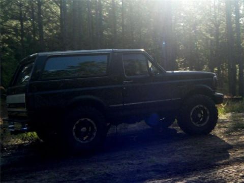 1994 Ford Bronco - Side view of a 1994 Ford Bronco on a muddy dirt road surrounded by trees.