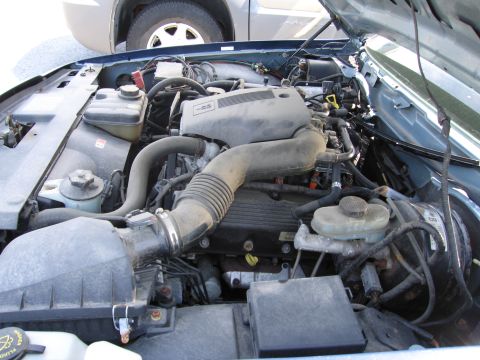 1991 Ford LTD Crown Victoria - The engine bay of a blue vehicle is shown, with another vehicle partially visible in the background.
