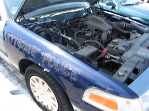 1991 Ford LTD Crown Victoria - A blue police car with its hood open, revealing the engine compartment and text on the fender.
