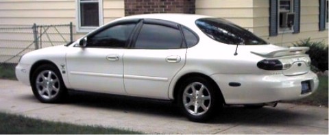 1997 Ford Taurus - This white sedan is parked in front of a house with a fence and some bushes.