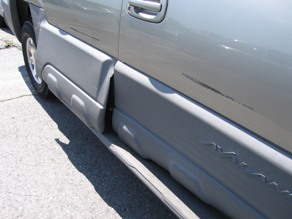 Side of a gray Chevrolet Avalanche showing the lower body cladding and a scratch on the door