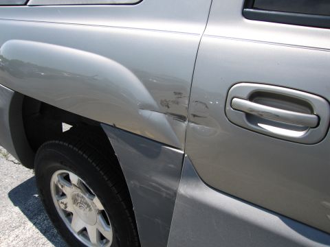 1991 Ford LTD Crown Victoria - Damage to the rear quarter panel of a silver SUV, affecting the area around the door handle.