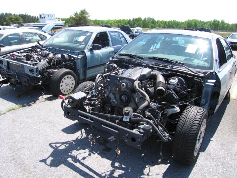 1991 Ford LTD Crown Victoria - Two stripped 1991 Ford Crown Victoria LTDs sit in a junkyard, their engines exposed and body panels removed.
