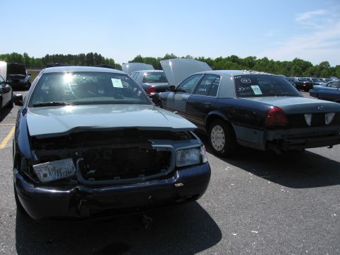 1991 Ford LTD Crown Victoria - Two sedans are parked in an outdoor lot, one with its hood open and front-end damage.